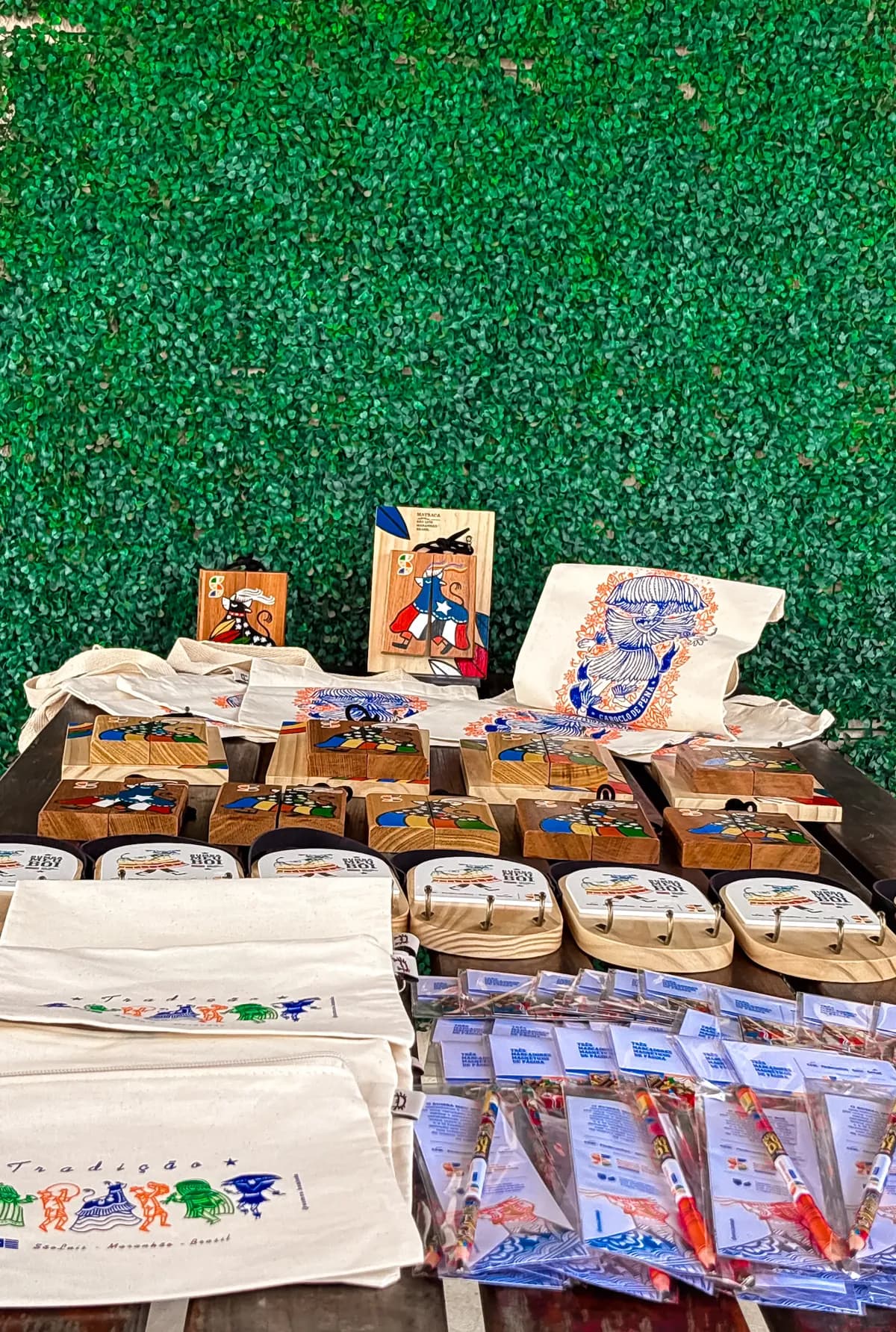 Banca da Kambada em feira, com matracas pintadas à mão, ecobags e marcadores de página expostos